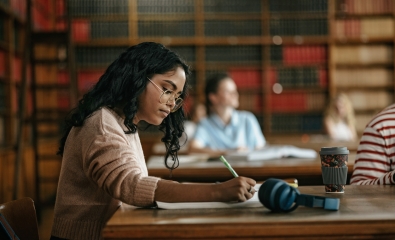 Student writing on notepad in a college library