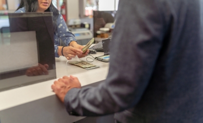 Bank teller counts out cash to man in suit jacket 