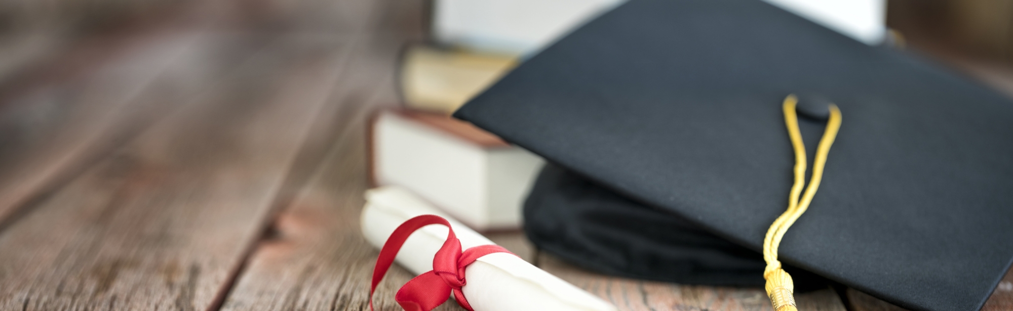 Graduation theme, a diploma and grad cap with a stack of books on a wooden table