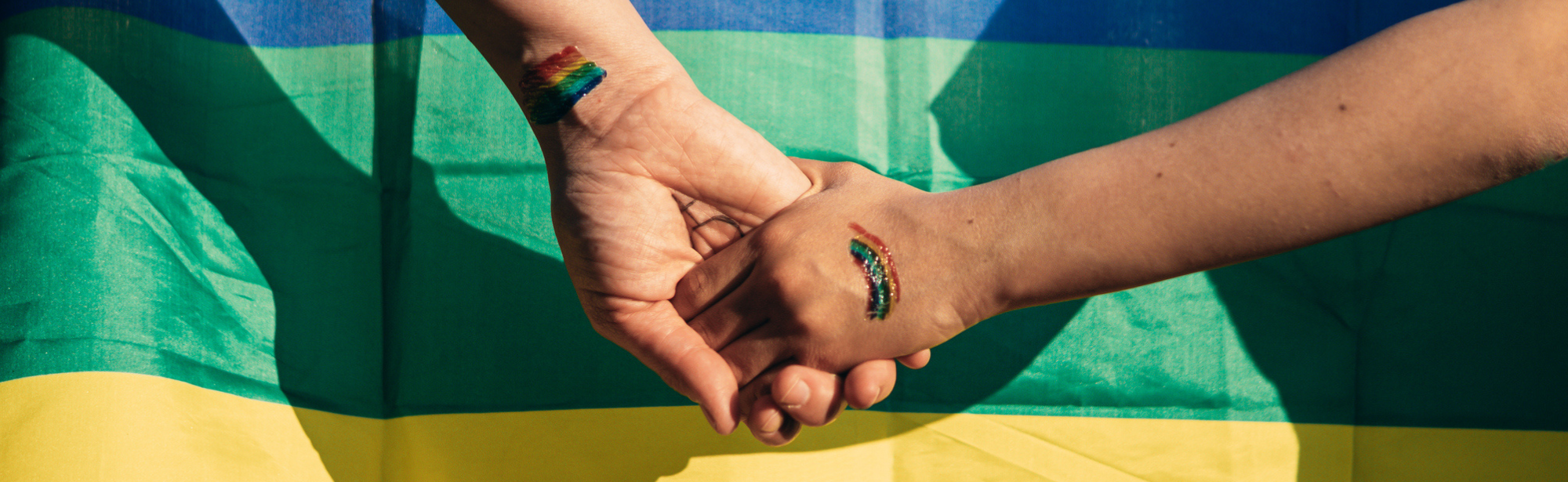 Two people holding hands in front of rainbow flags with temp rainbow tattoos