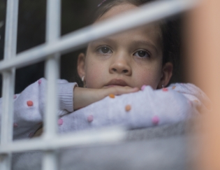 Sad young girl looking through a window with bars